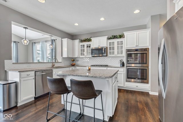 kitchen with appliances with stainless steel finishes, glass insert cabinets, white cabinets, and decorative light fixtures