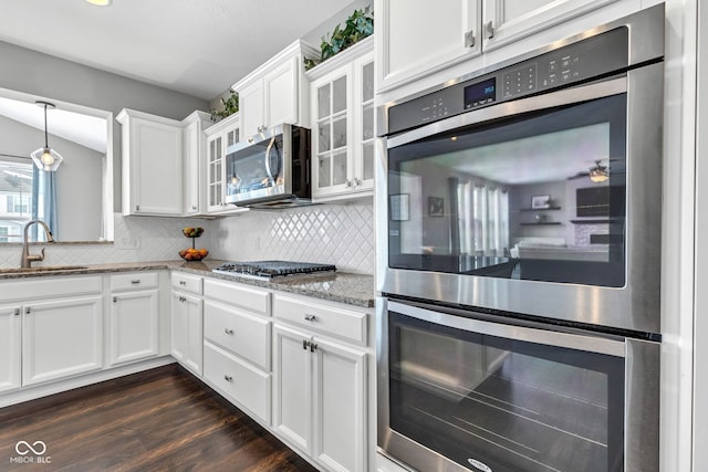 kitchen featuring white cabinets, glass insert cabinets, light stone counters, appliances with stainless steel finishes, and a sink