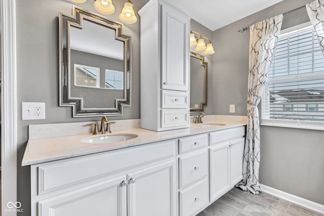 full bath featuring double vanity, a sink, and baseboards