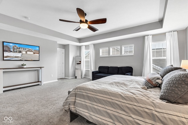 bedroom with a ceiling fan, a raised ceiling, light carpet, and baseboards