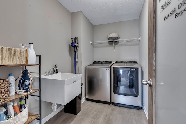 washroom with laundry area, light wood finished floors, a textured ceiling, washing machine and dryer, and a sink