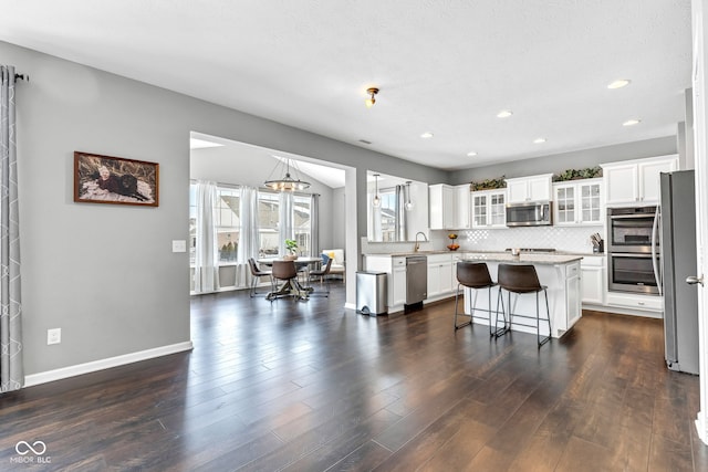 kitchen featuring stainless steel appliances, a kitchen island, light countertops, a kitchen bar, and glass insert cabinets