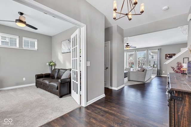 interior space featuring ceiling fan with notable chandelier, dark wood-style flooring, and baseboards