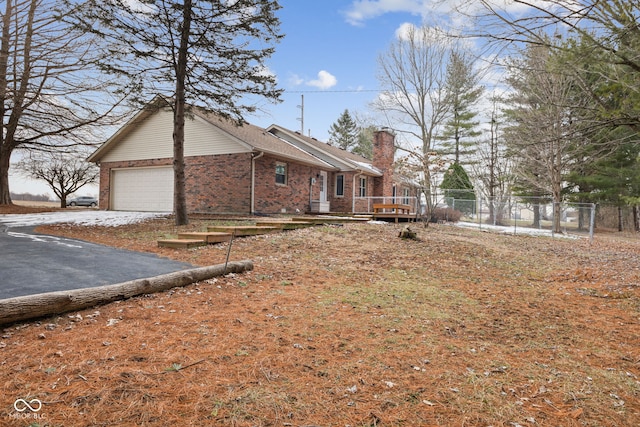 view of side of property featuring aphalt driveway, an attached garage, brick siding, fence, and a chimney