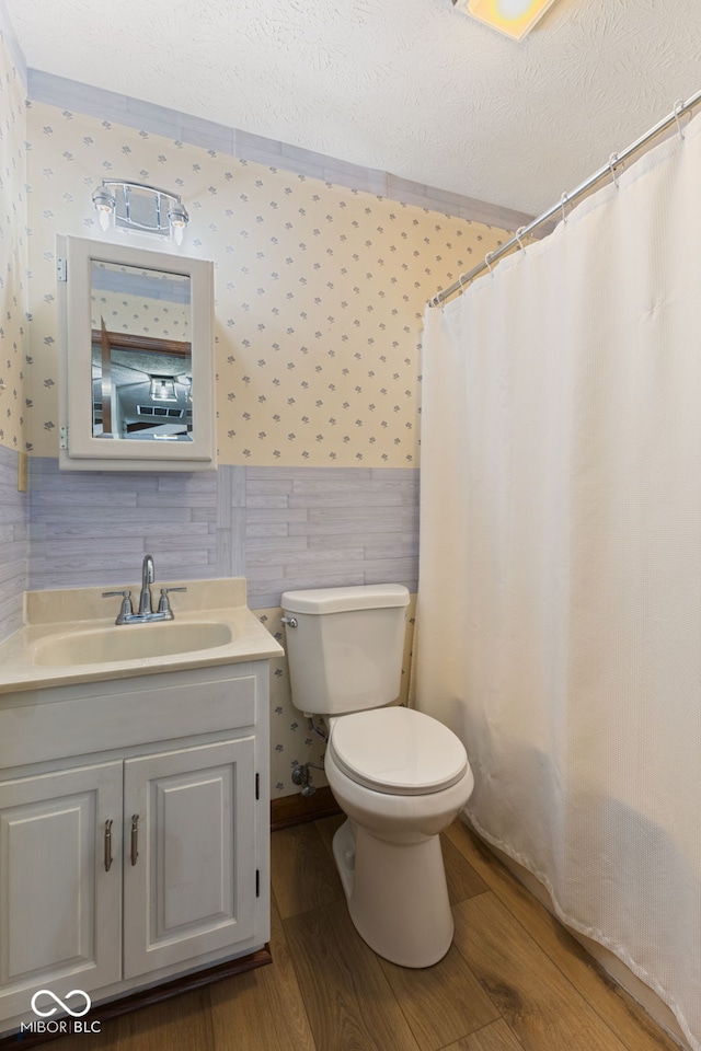 full bathroom with wood finished floors, wainscoting, toilet, and wallpapered walls