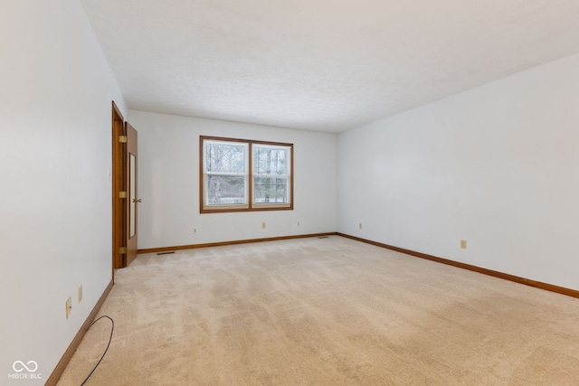 empty room with light carpet, baseboards, and a textured ceiling