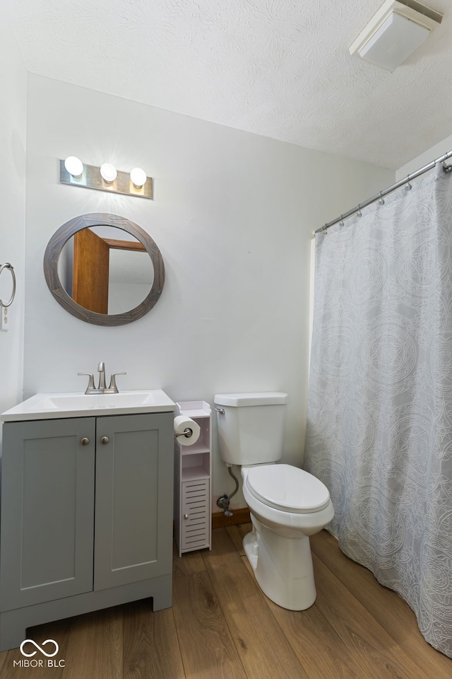 full bathroom with toilet, a textured ceiling, vanity, and wood finished floors