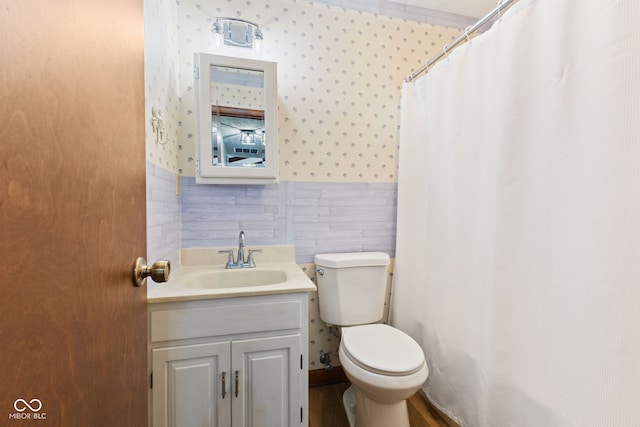 bathroom featuring toilet, a wainscoted wall, tile walls, vanity, and wallpapered walls