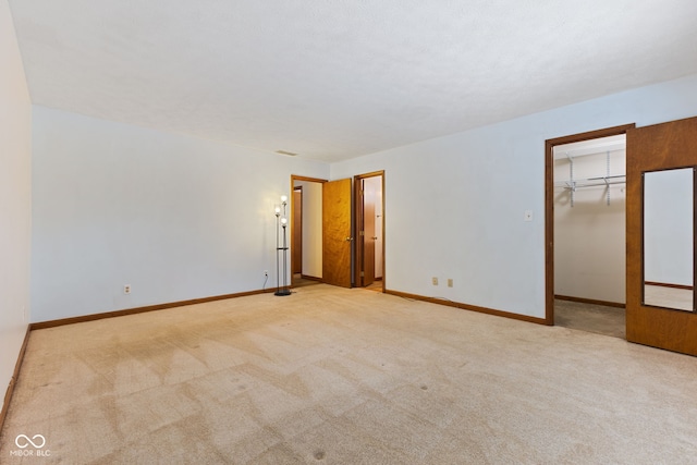 unfurnished bedroom featuring a walk in closet, light carpet, and baseboards