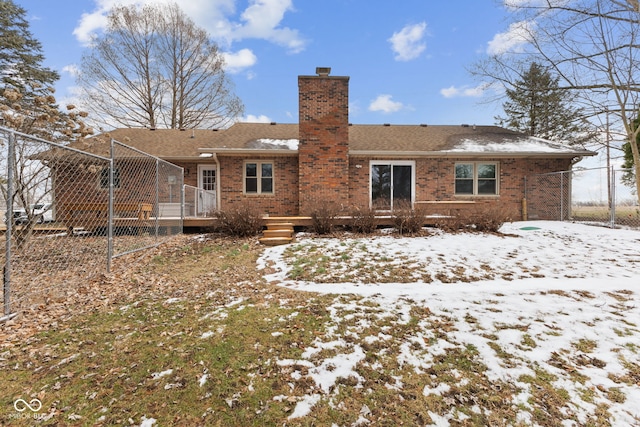 snow covered house with brick siding, fence, and a chimney