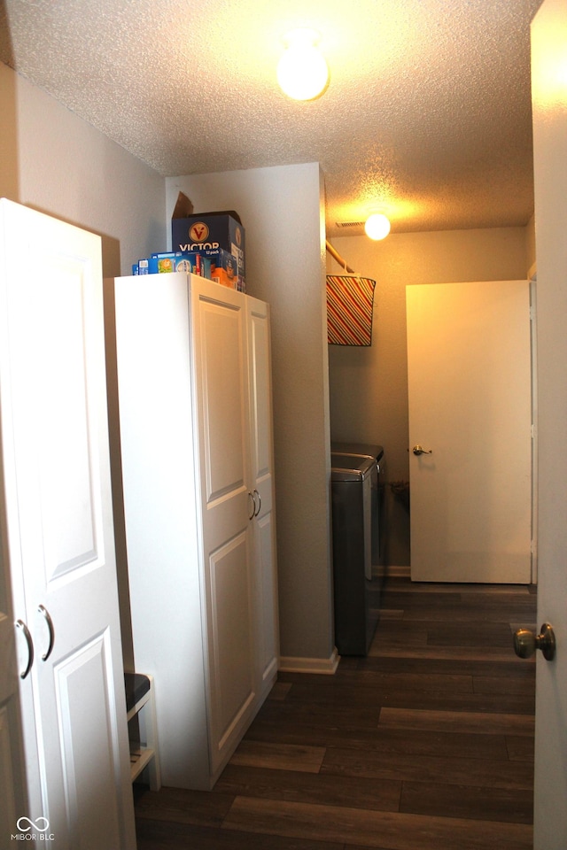 corridor with a textured ceiling, dark wood-type flooring, and washer and clothes dryer