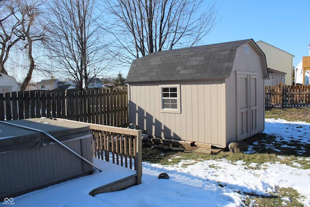 snow covered structure with a storage shed, an outbuilding, fence private yard, and a hot tub