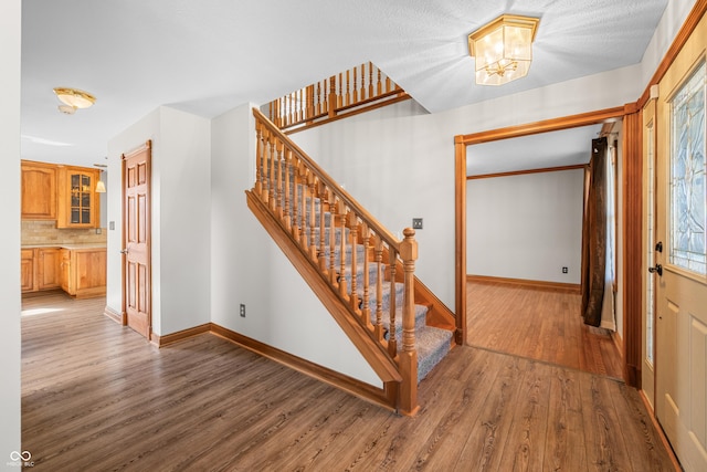 stairway with an inviting chandelier, baseboards, and wood finished floors