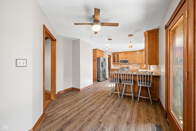 kitchen with a peninsula, wood finished floors, visible vents, appliances with stainless steel finishes, and glass insert cabinets