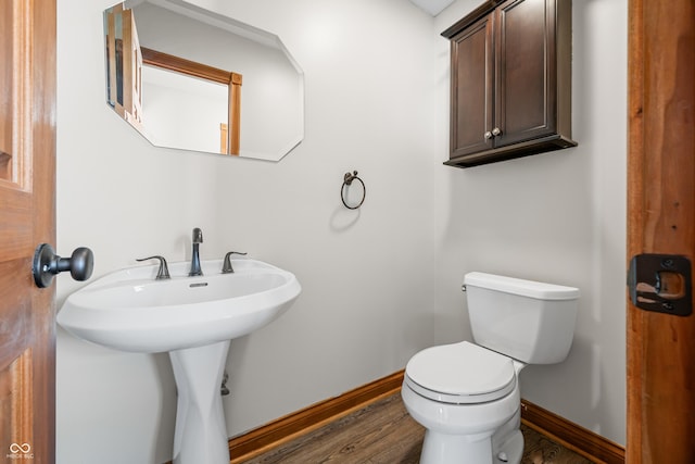 half bath with toilet, baseboards, and wood finished floors