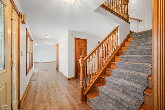 stairs with wood-type flooring, visible vents, and baseboards