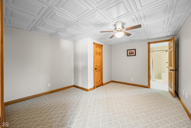 empty room with light carpet, a ceiling fan, an ornate ceiling, and baseboards