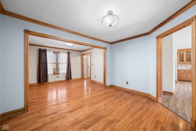 spare room with a textured ceiling, light wood-style flooring, visible vents, baseboards, and crown molding