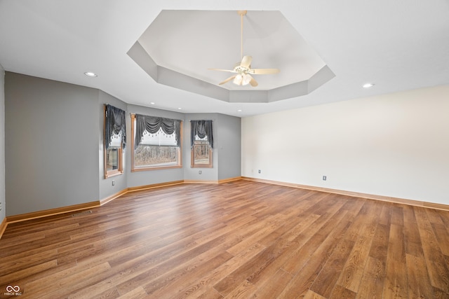 spare room with ceiling fan, recessed lighting, wood finished floors, baseboards, and a tray ceiling