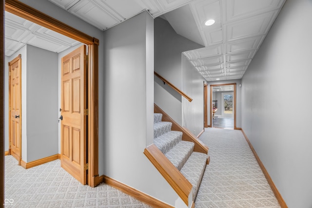 hall with stairway, baseboards, and light colored carpet