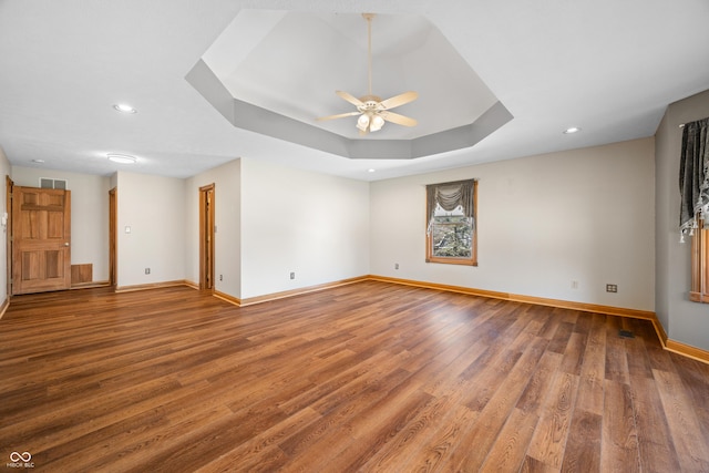 empty room with wood finished floors, a raised ceiling, visible vents, and baseboards