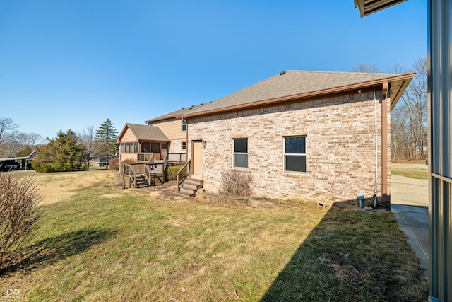 rear view of property with a yard, roof with shingles, and brick siding