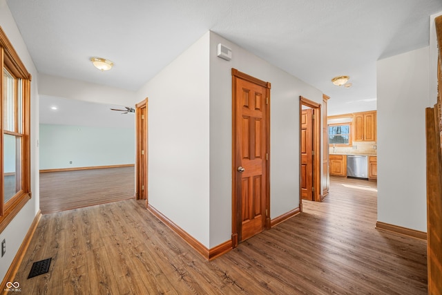 hall with baseboards, visible vents, and wood finished floors