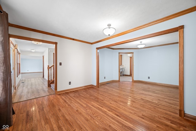 unfurnished room with stairs, crown molding, wood finished floors, and baseboards