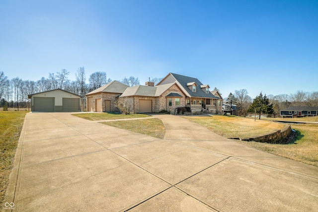 view of front of property featuring an outbuilding, covered porch, a detached garage, stone siding, and a front yard