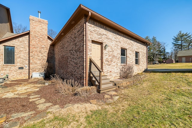 view of home's exterior with entry steps, brick siding, a yard, and a chimney