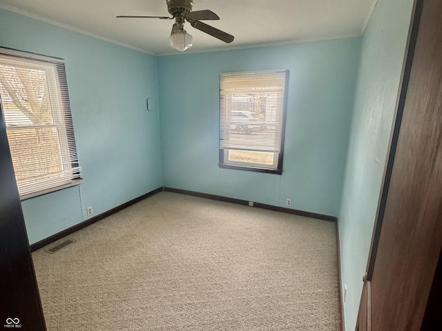 carpeted empty room featuring ceiling fan, ornamental molding, visible vents, and baseboards