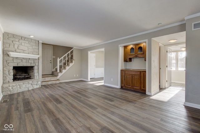 unfurnished living room featuring a stone fireplace, stairway, baseboards, and wood finished floors