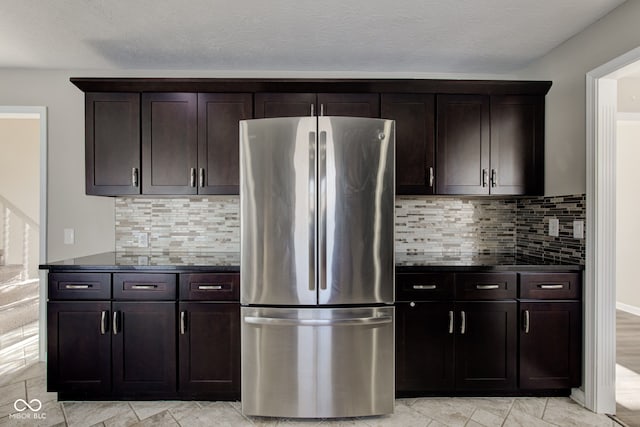 kitchen featuring backsplash, dark brown cabinets, and freestanding refrigerator