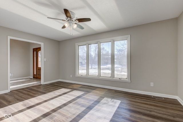 spare room with dark wood-style flooring, visible vents, ceiling fan, and baseboards