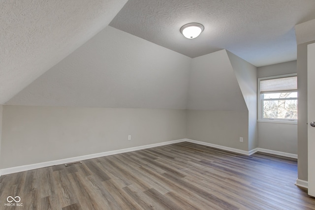 additional living space featuring lofted ceiling, a textured ceiling, wood finished floors, and baseboards