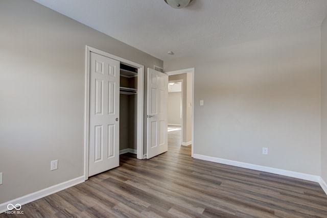 unfurnished bedroom featuring a textured ceiling, dark wood-style flooring, a closet, and baseboards