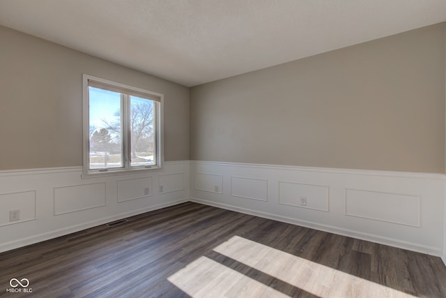 empty room featuring visible vents, dark wood-style flooring, and wainscoting