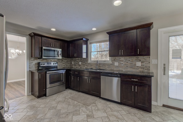 kitchen with dark brown cabinetry, tasteful backsplash, appliances with stainless steel finishes, dark stone countertops, and a sink