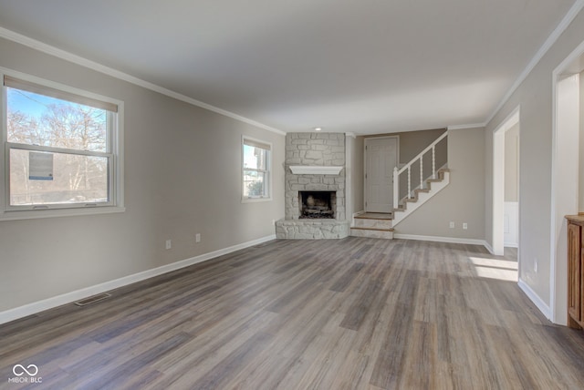 unfurnished living room featuring baseboards, stairway, ornamental molding, wood finished floors, and a stone fireplace