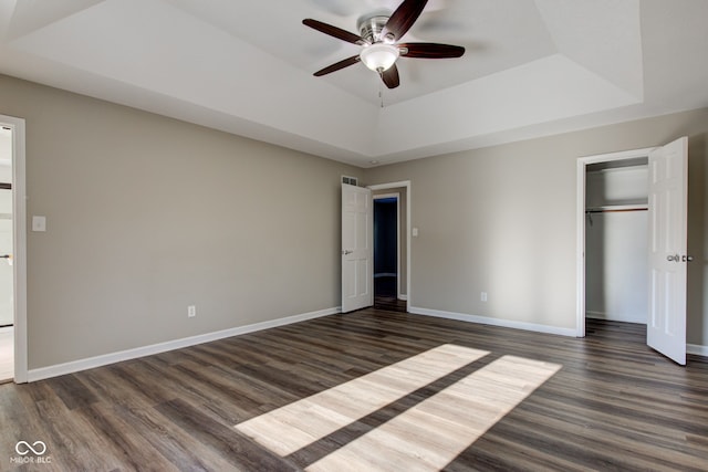 unfurnished bedroom featuring a raised ceiling, dark wood finished floors, and baseboards