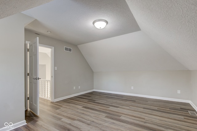 additional living space with lofted ceiling, visible vents, a textured ceiling, wood finished floors, and baseboards