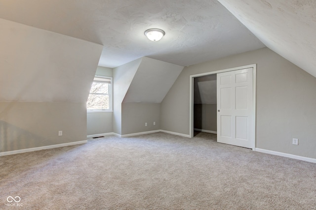 additional living space with visible vents, baseboards, lofted ceiling, a textured ceiling, and carpet flooring