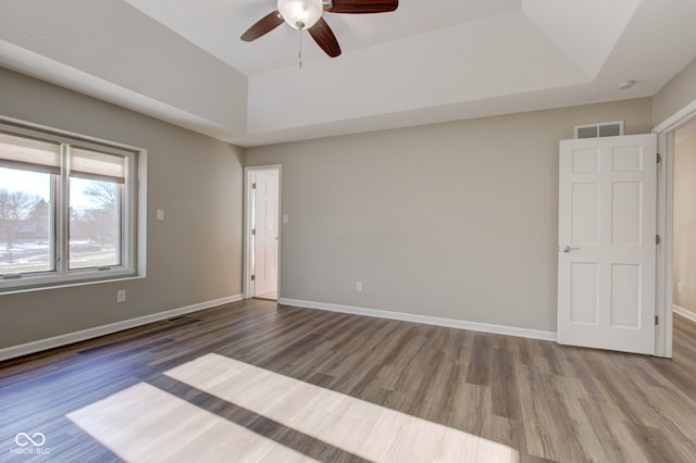 unfurnished room featuring a tray ceiling, visible vents, baseboards, and wood finished floors