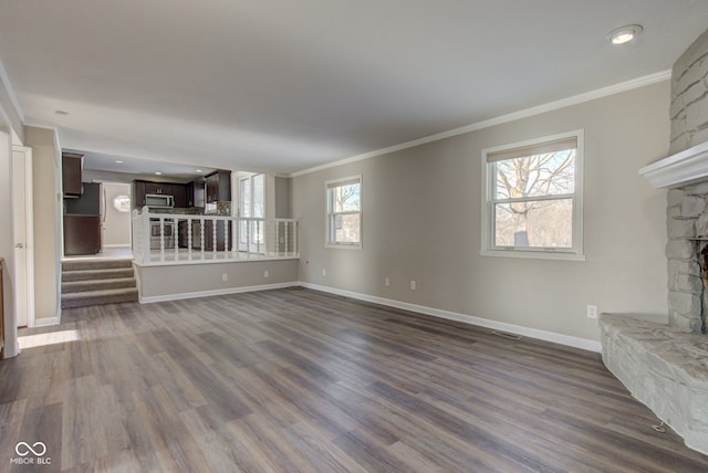 unfurnished living room with a stone fireplace, dark wood-style flooring, baseboards, ornamental molding, and stairway