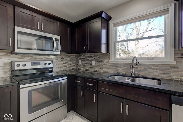 kitchen featuring dark brown cabinets, appliances with stainless steel finishes, dark stone counters, and a sink