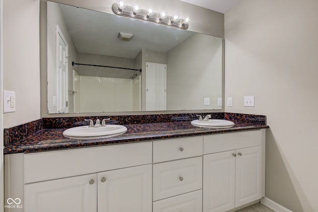 full bath with double vanity, baseboards, a shower, and a sink