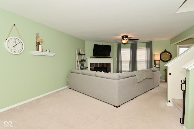 living area featuring a fireplace, light colored carpet, ceiling fan, baseboards, and stairs