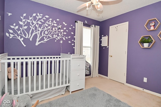 bedroom with a textured ceiling, a crib, carpet flooring, and baseboards