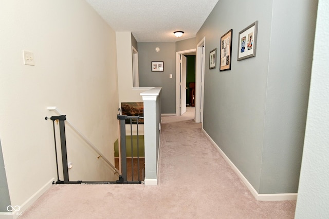 hallway featuring baseboards, carpet flooring, a textured ceiling, and an upstairs landing