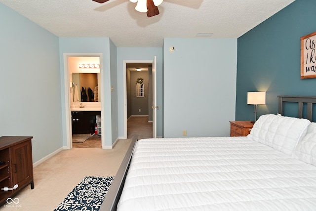 bedroom featuring baseboards, connected bathroom, light colored carpet, ceiling fan, and a textured ceiling